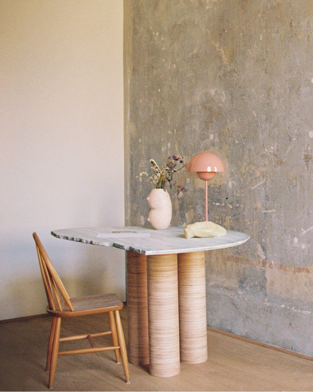 Modern dining table with marble top and wooden base against a textured wall.